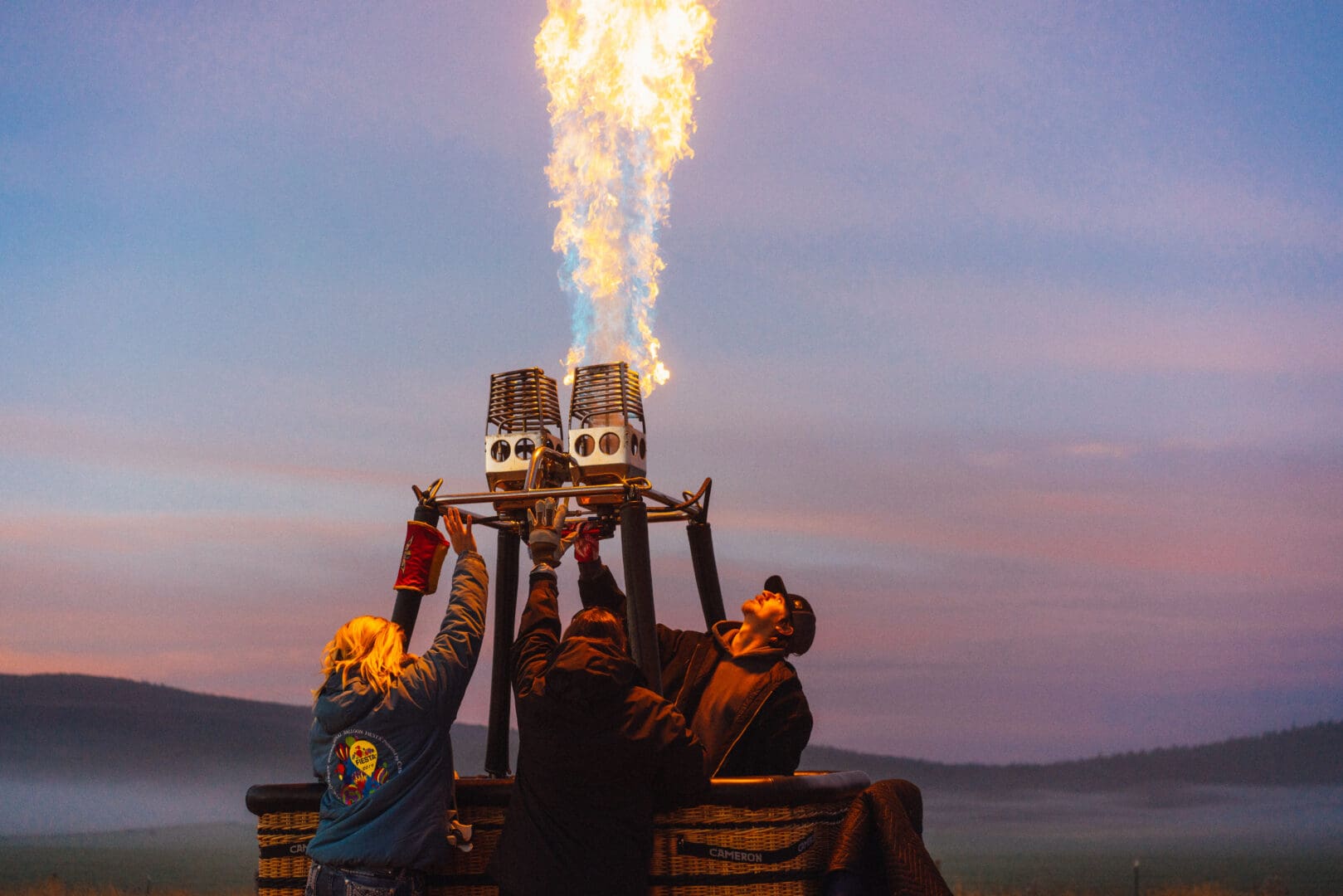 Three workers setting up a hot air balloon with flames shooting through the top of it.