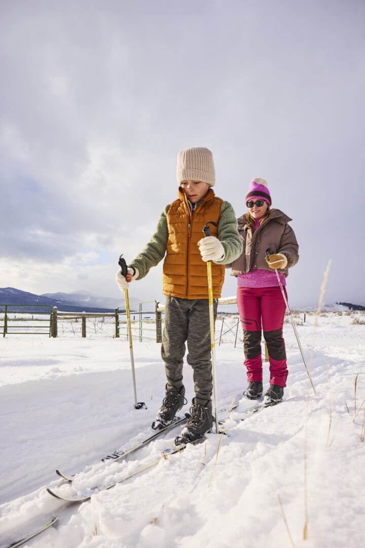 Child and his mother cross-country skiing outside on a snowy trail.