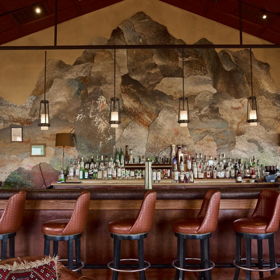 Bar chairs at a bar with a mountain western painting in the background.
