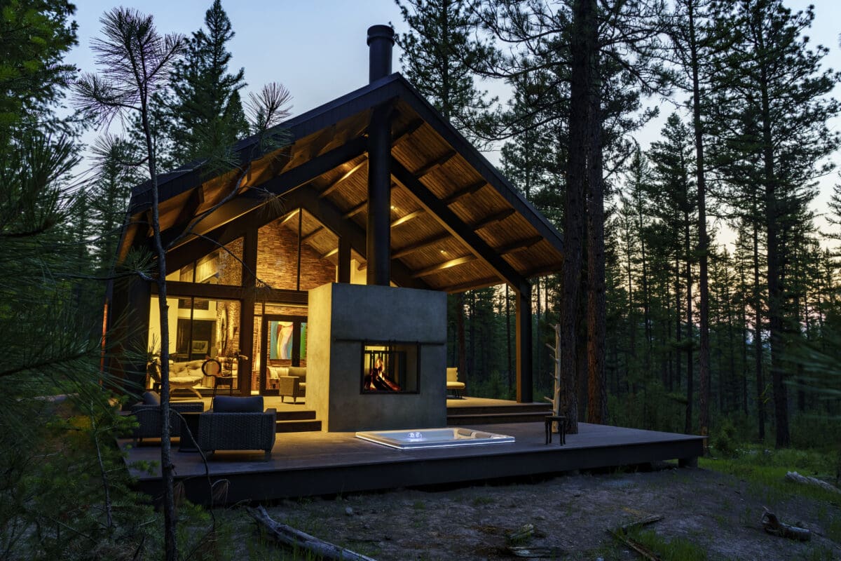 A glass home surrounded by trees at dusk.