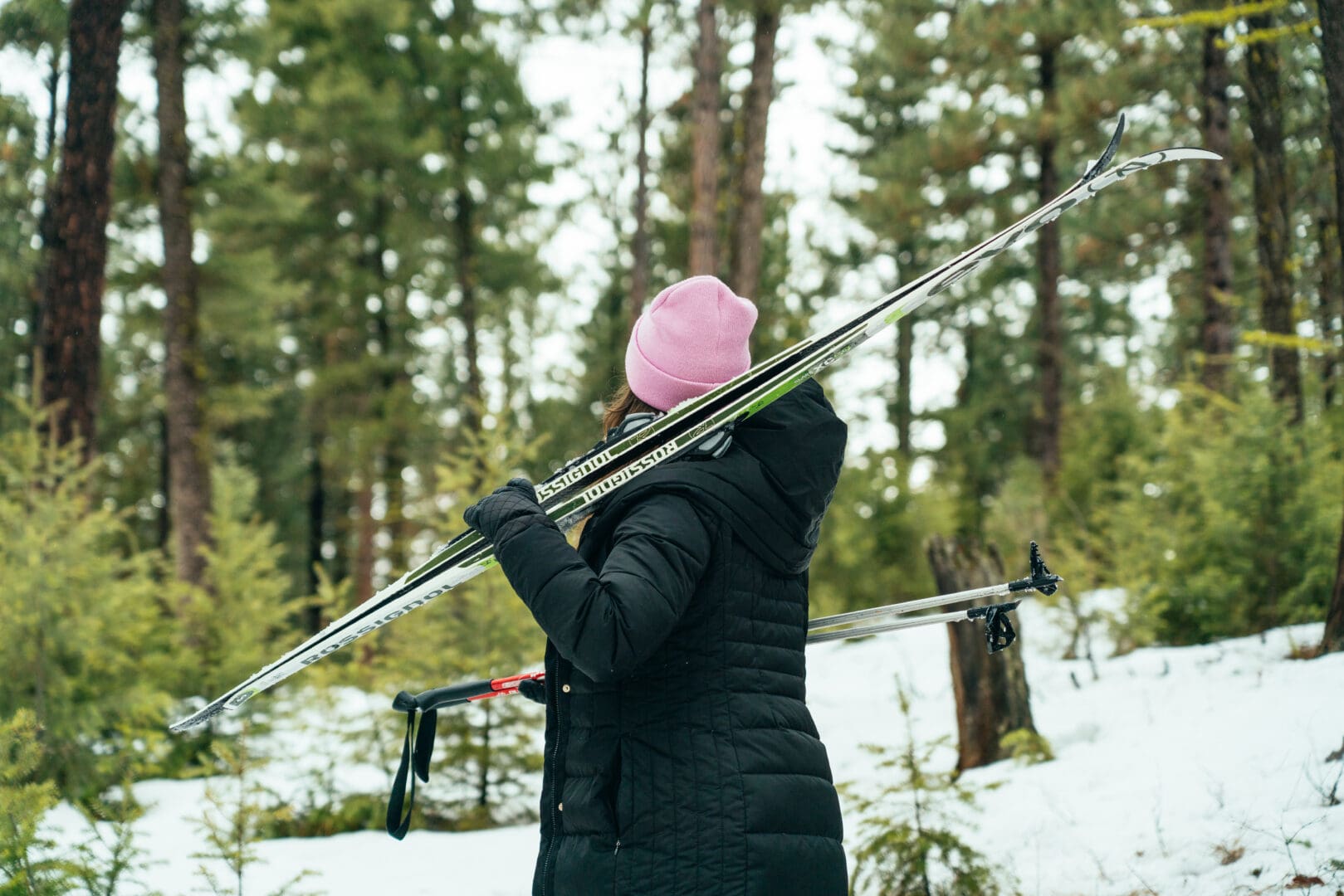 Woman walking outside in a forest holding cross-country skis.
