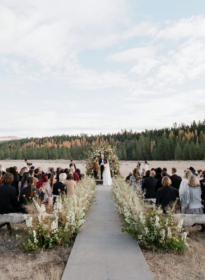An outdoor wedding with flowers lining the aisle.