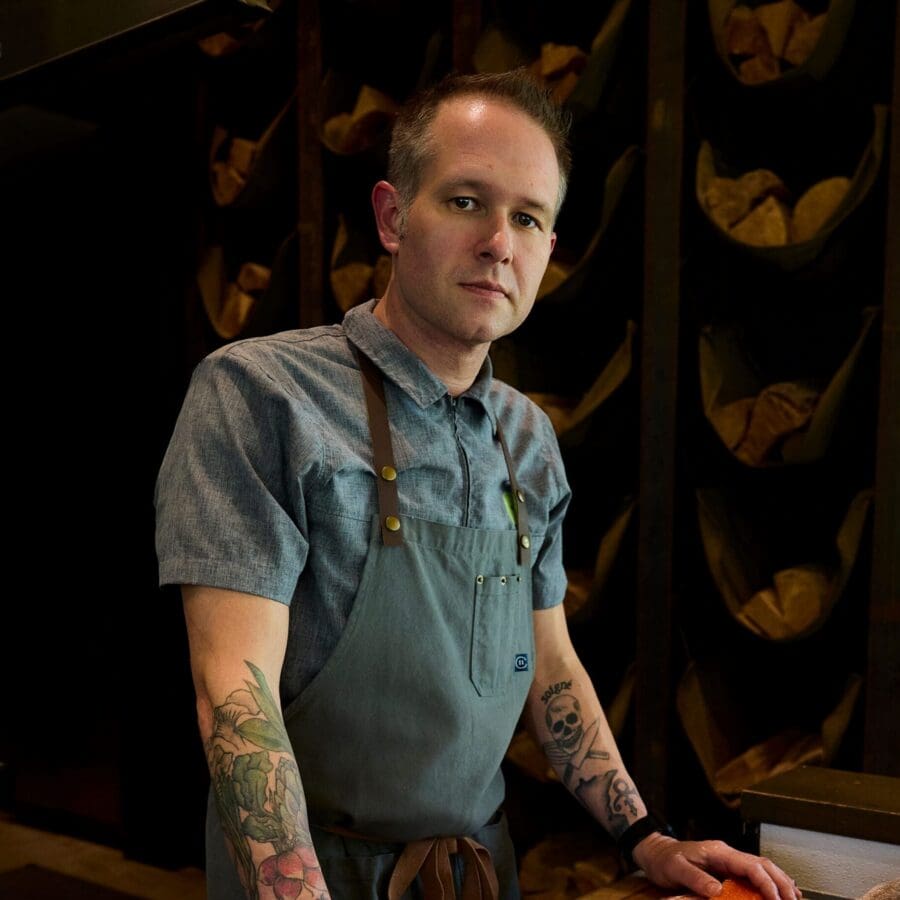 Chef standing next to cut up salmon on a cutting board in a dark elegant dining room.
