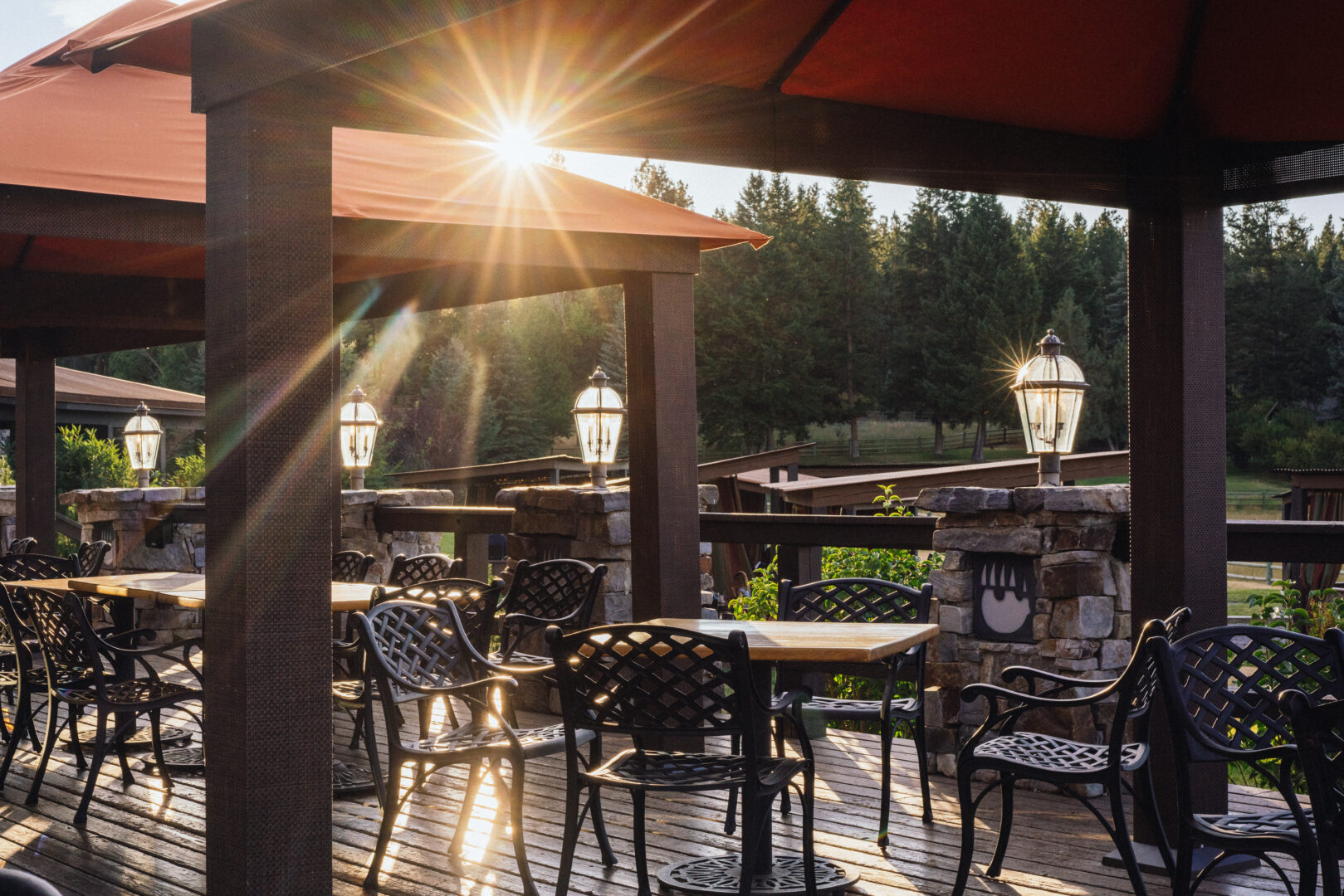 A view of an outside deck with tables and light shining through a red umbrella.