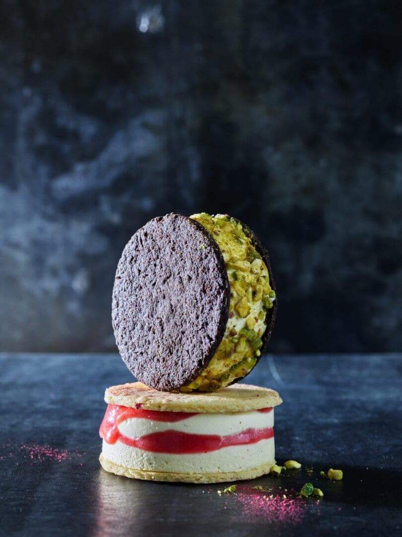 Two ice cream sandwiches, one chocolate, one vanilla, on a table with a dark background.