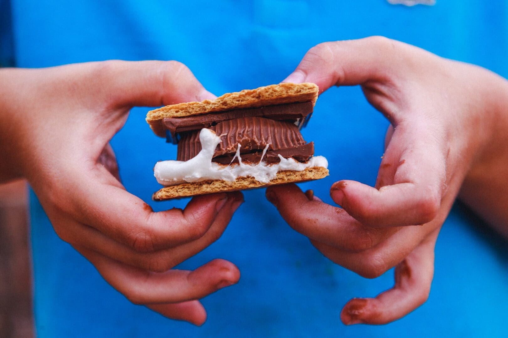 Closeup of a child holding a smores with a Reeces peanut butter cup.