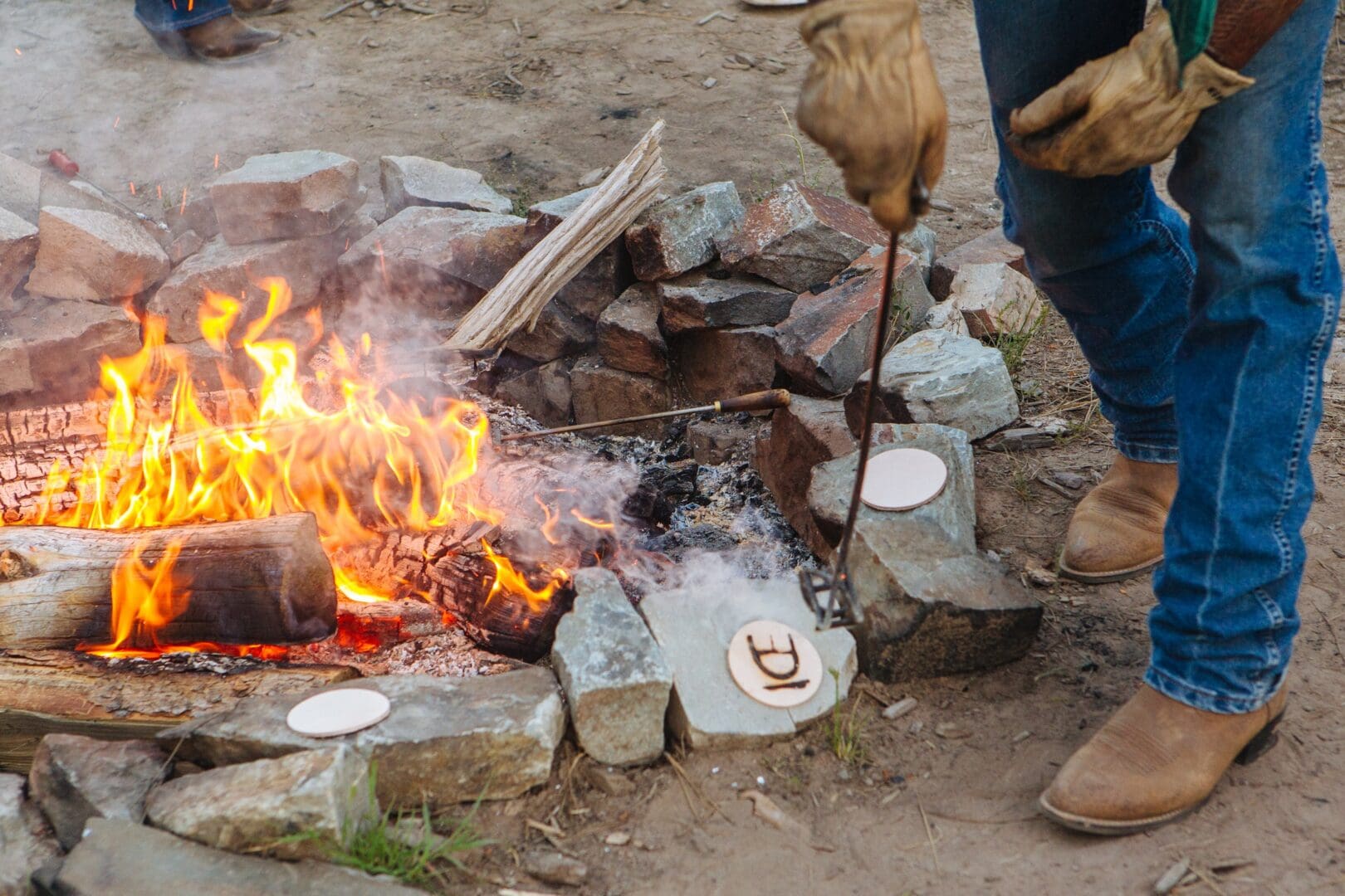 Man tending to a fire and branding pieces of wood with a brand.