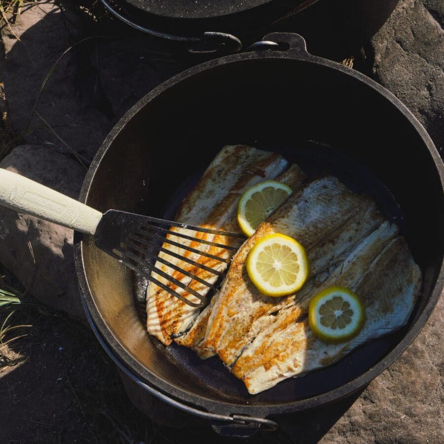 Fish being cooked in a cast iron skillet with lemon slices.