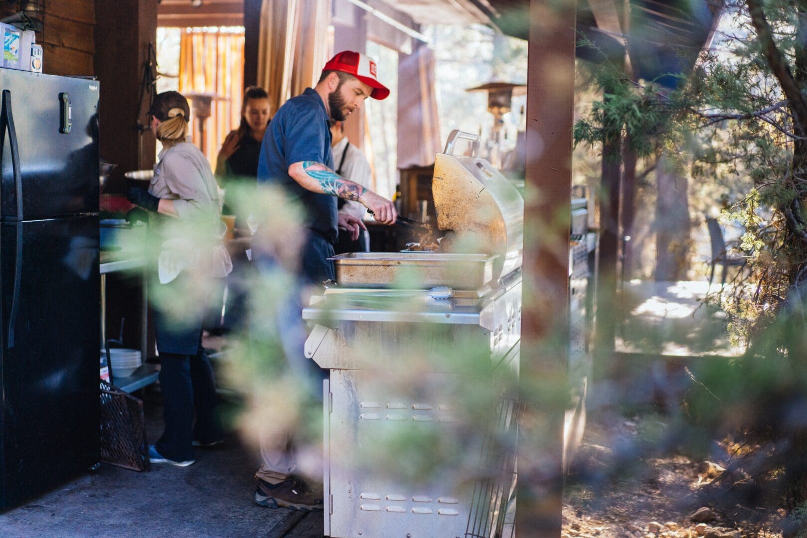 Chef cooking outside of a dining pavilion wearing a baseball cap.