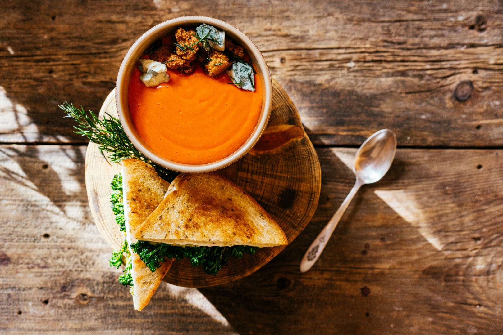 A bowl of tomato soup with a grilled cheese on a wooden table.