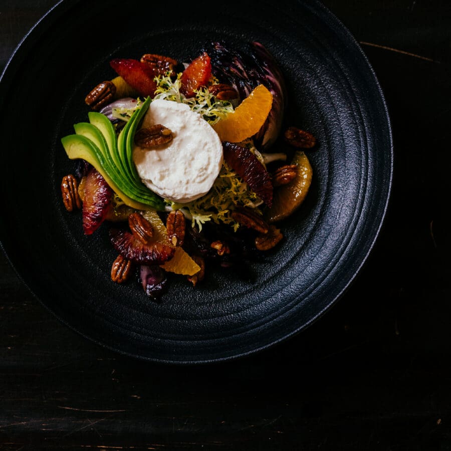 A food dish in a black bowl with avocado, meat, and toppings.