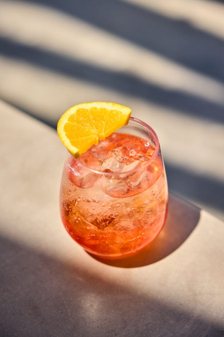 An orange cocktail with an orange slice.