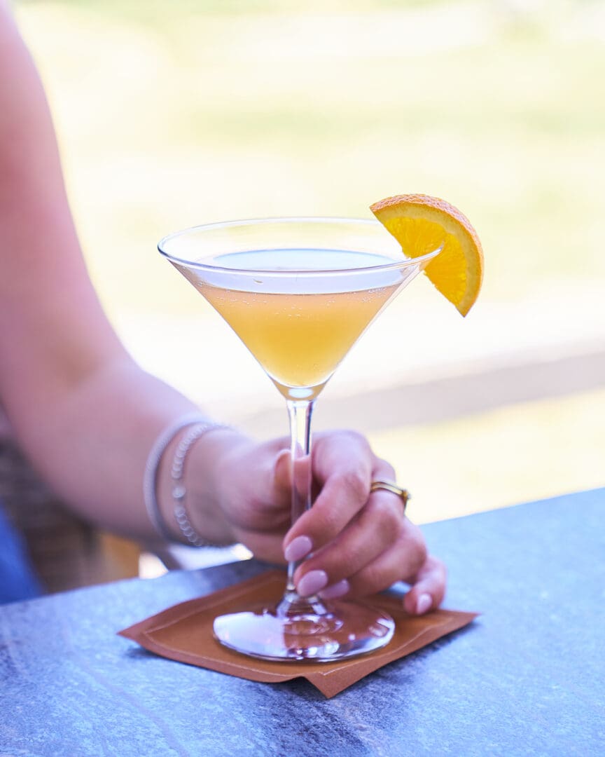 Woman's hand holding an orange cocktail with an orange slice on the top of it.
