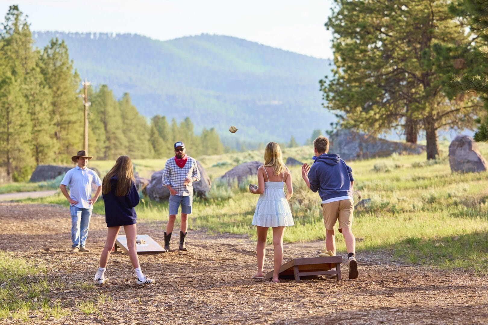 Family playing corn hole outside with mountains in the background.