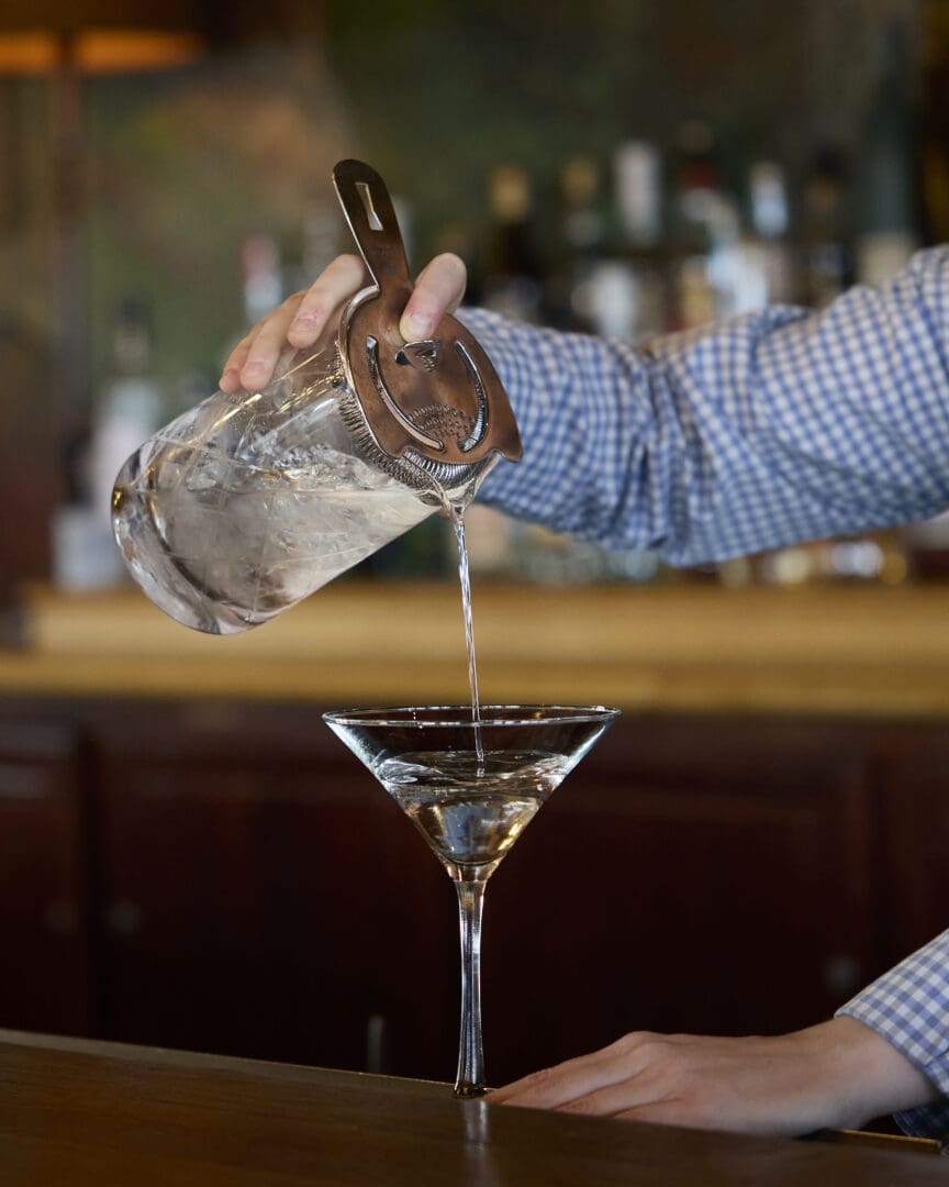 Bartender pouring alcohol from a shaker into a martini glass.