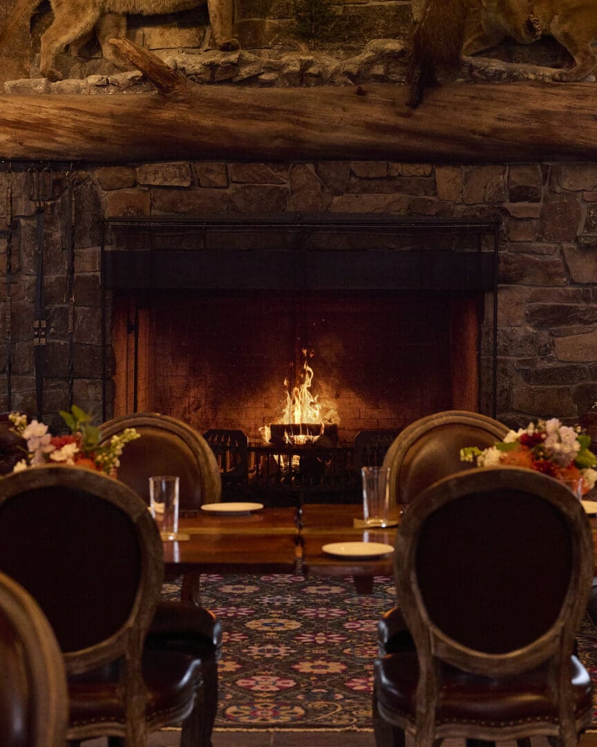 Two furnished chairs in front of a stone fireplace with a roaring fire.