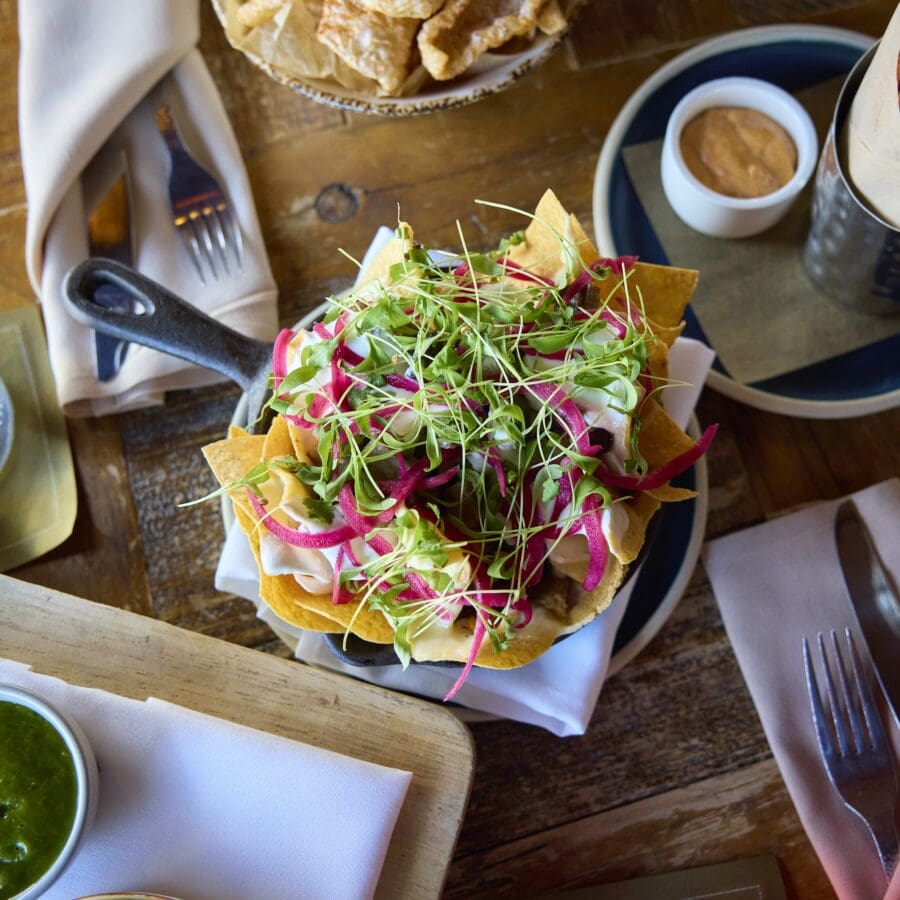 An array of food placed at a wooden table including nachos, fries, and dips.