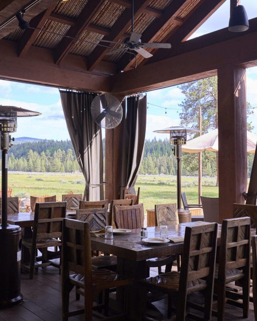 Inside of a dining pavilion with wooden tables and chairs and a view of outside mountains.