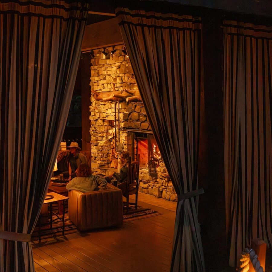 Group of people dining inside of a dimly lit pavilion outside with curtains leading to the entrance.