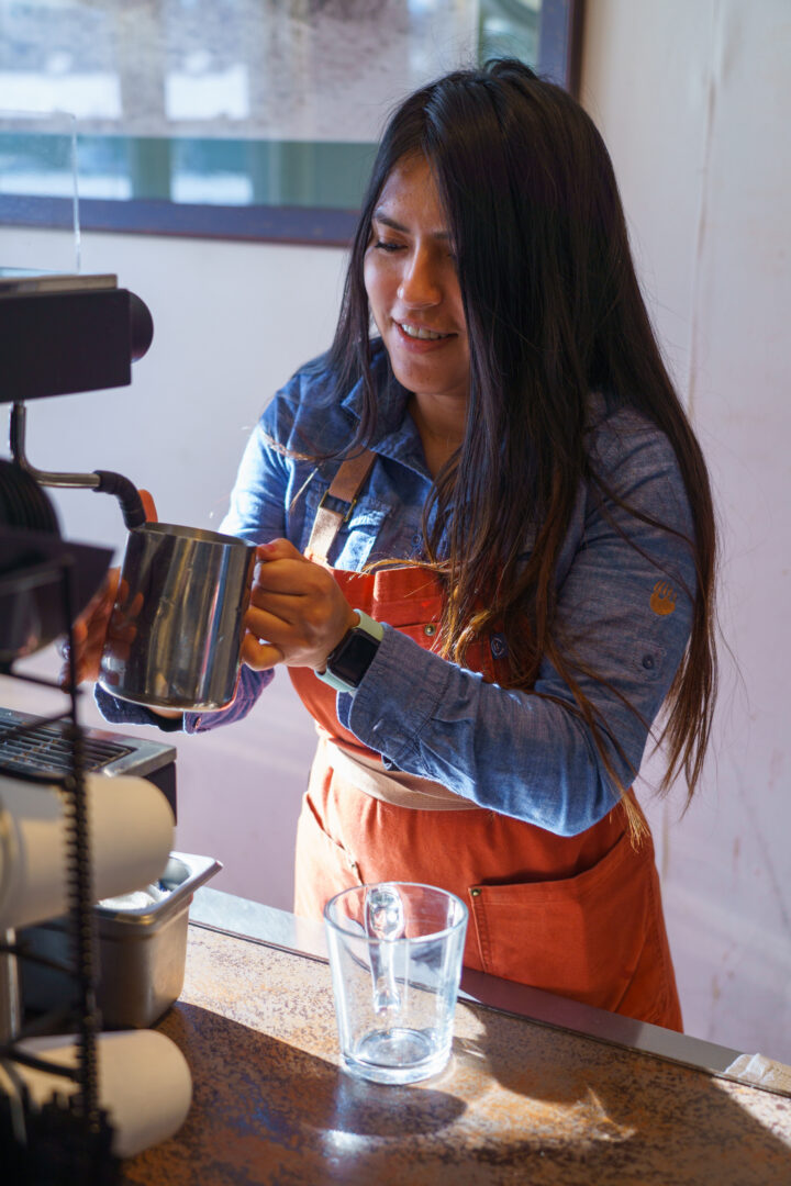 A barista in an orange apron making a latte.