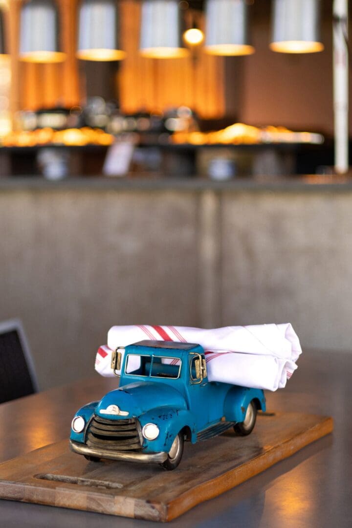 Toy blue truck at a restaurant table holding napkins.