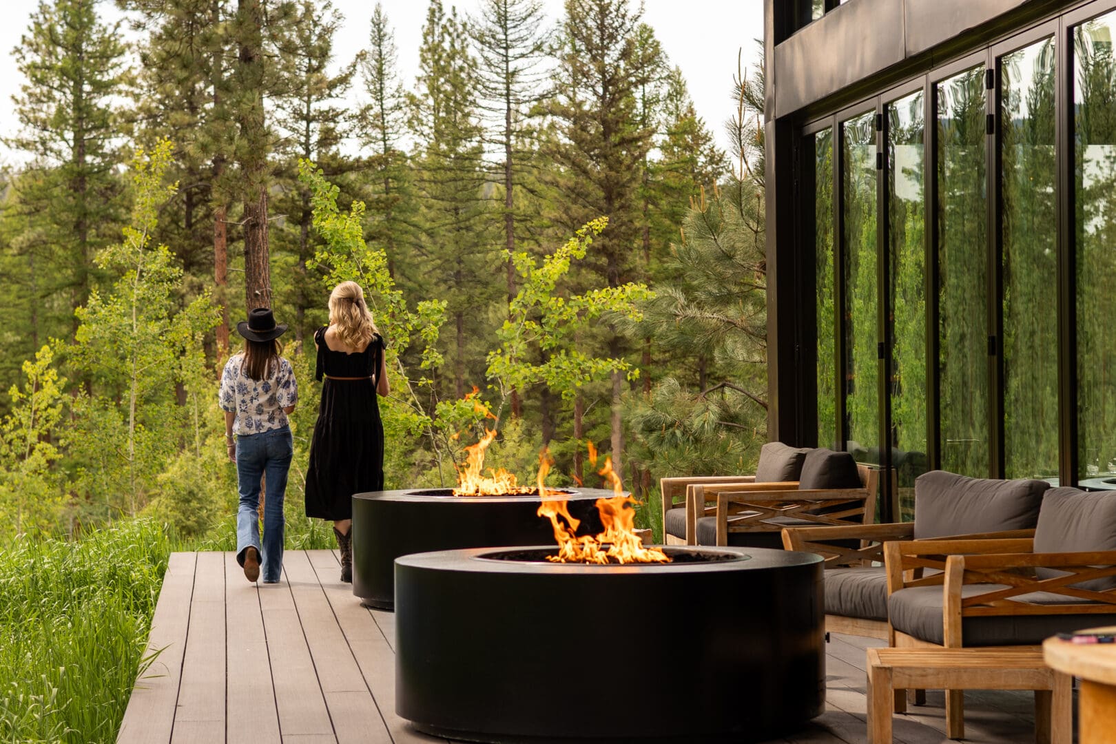 Two women walking along a wooden patio with chairs and two active charcoal fires.