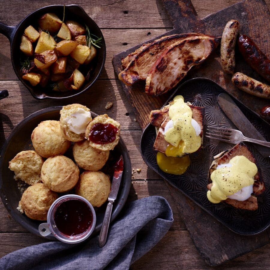 Biscuits, jam, sausages, and potatoes laid out on a wooden table.