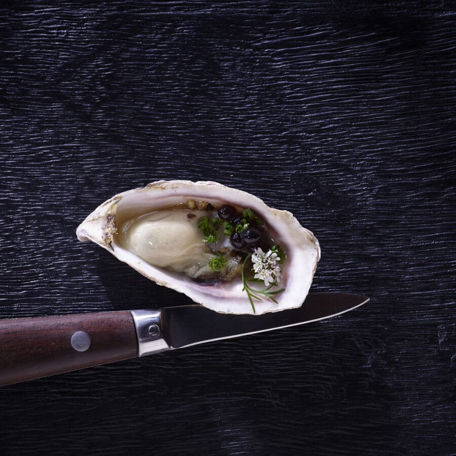Oyster on a black table with a knife next to it.