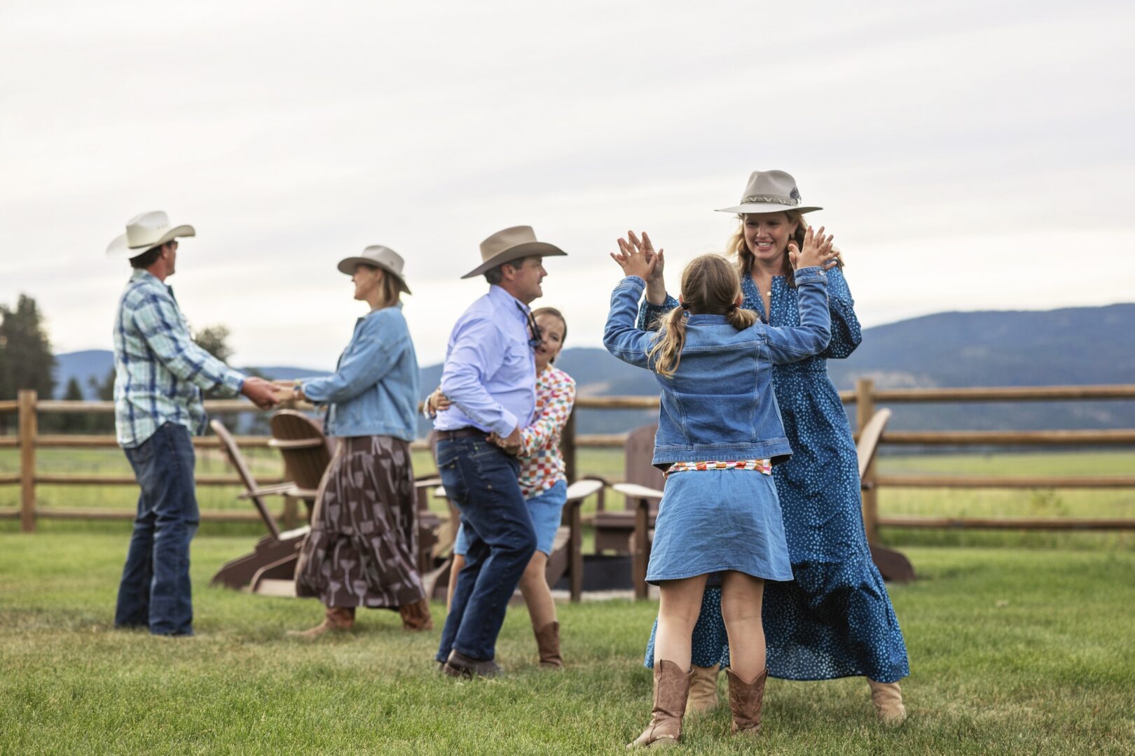 Family dancing on a green lawn with a wooden fence and field behind them.