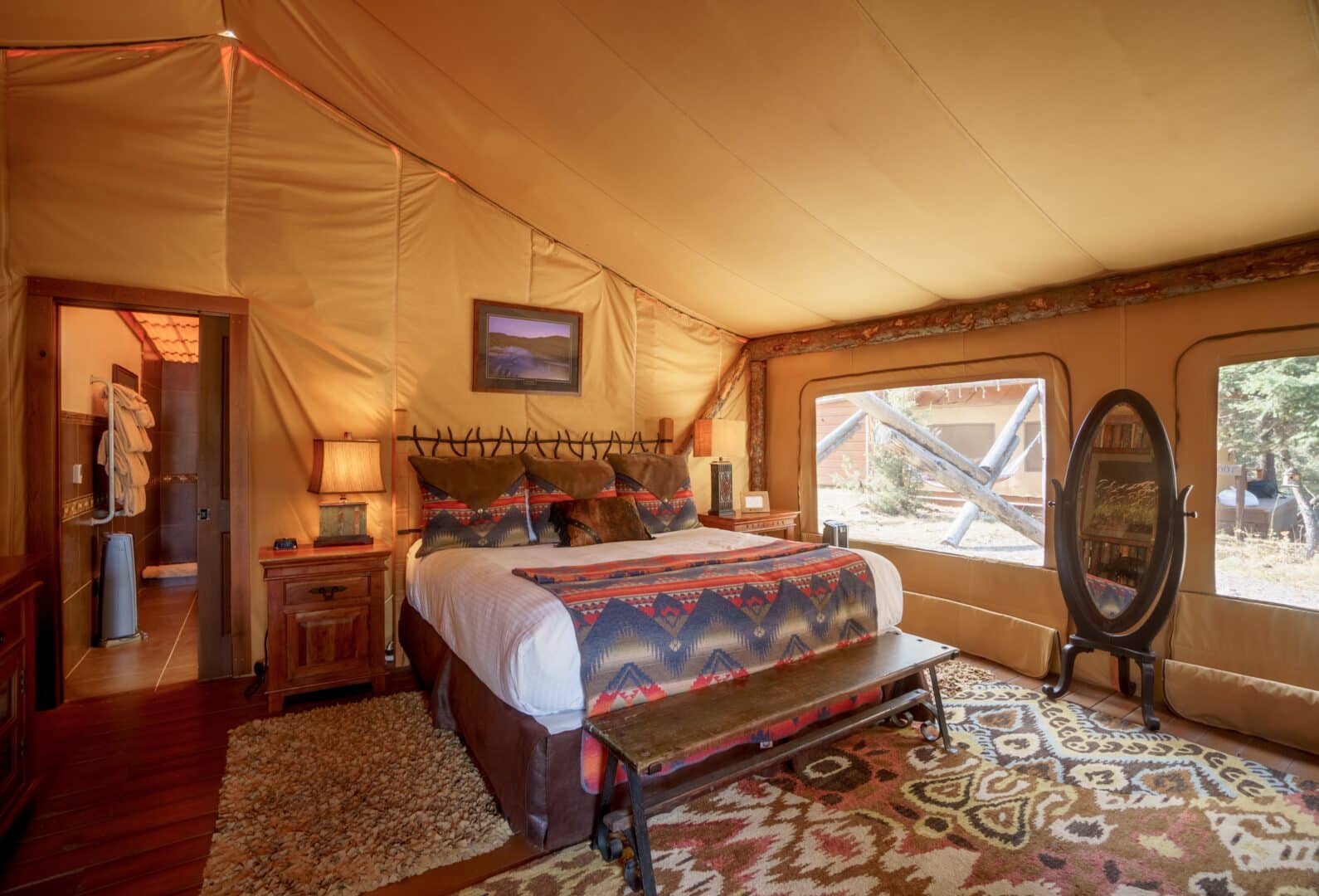 Inside of a western themed glamping tent with a large bed and door to a bathroom.