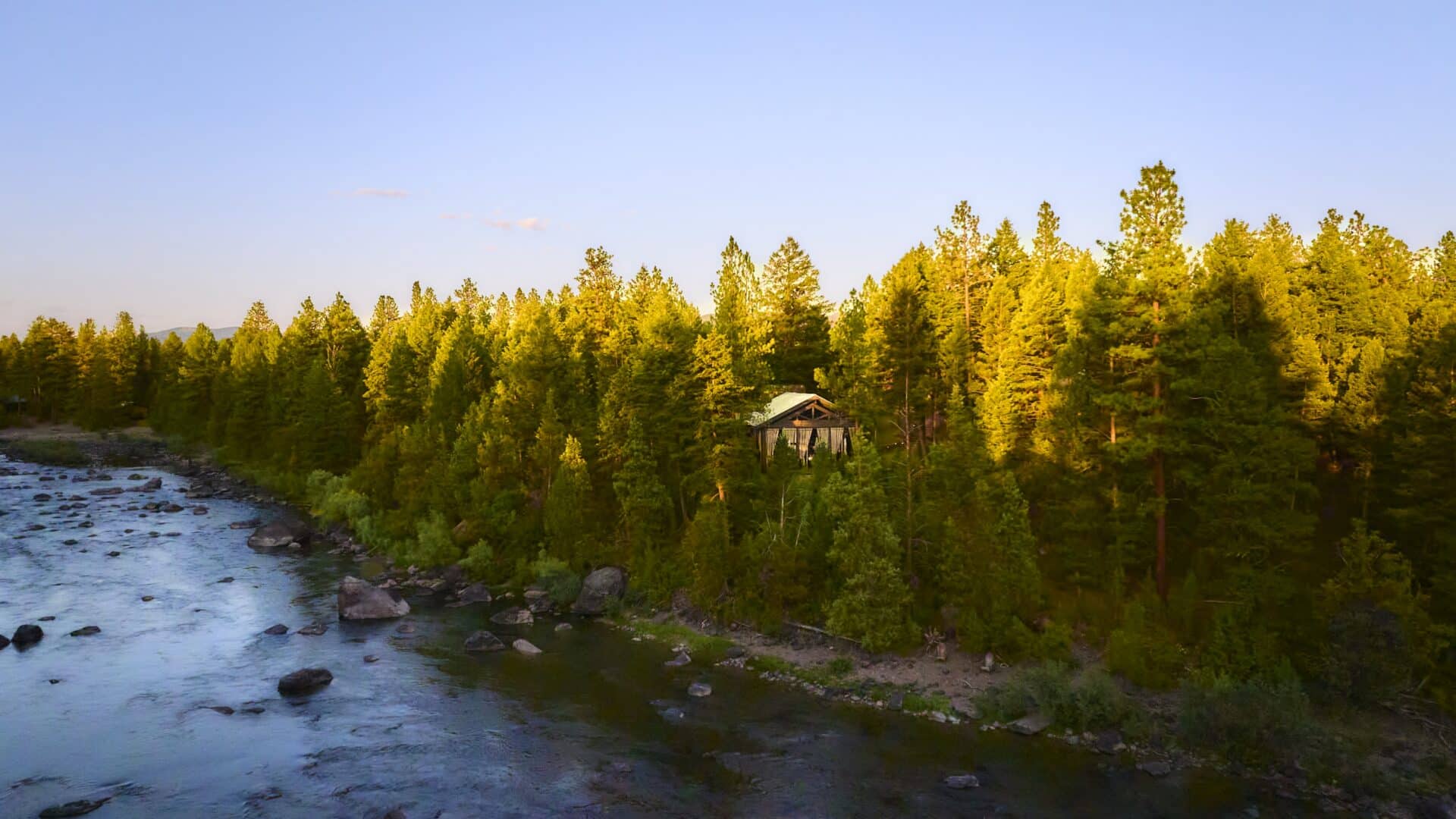 A pavilion sitting on the edge of a cliff with trees surrounding it and a flowing river below.