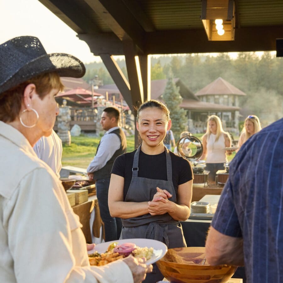 Chef standing under a pavilion outside preparing dishes for guests.