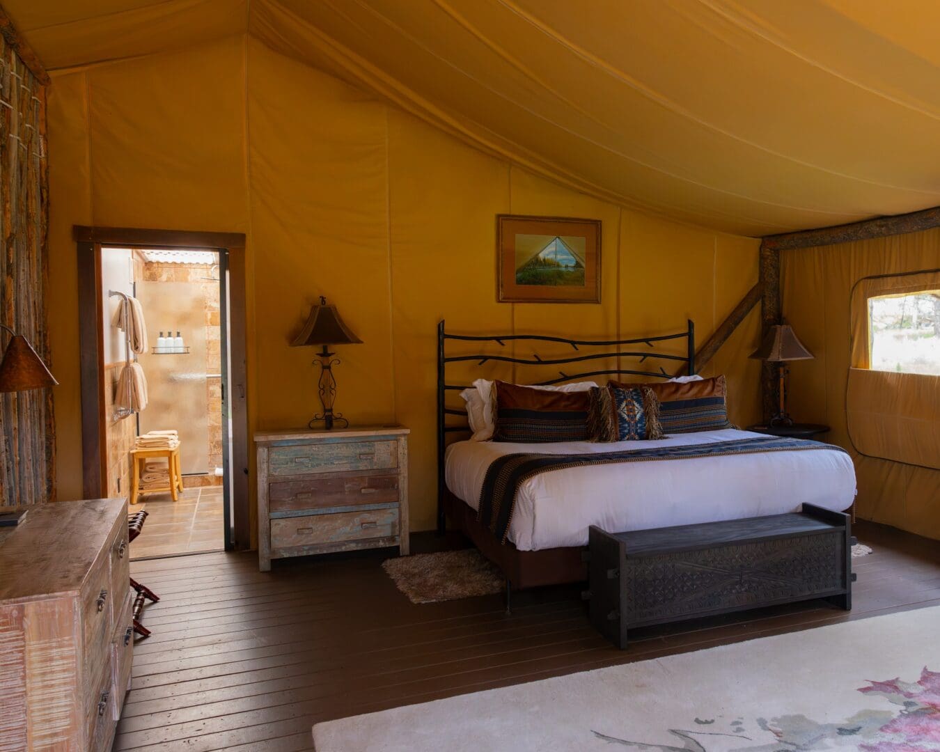 Inside of a western themed glamping tent with a large bed and door to a bathroom.