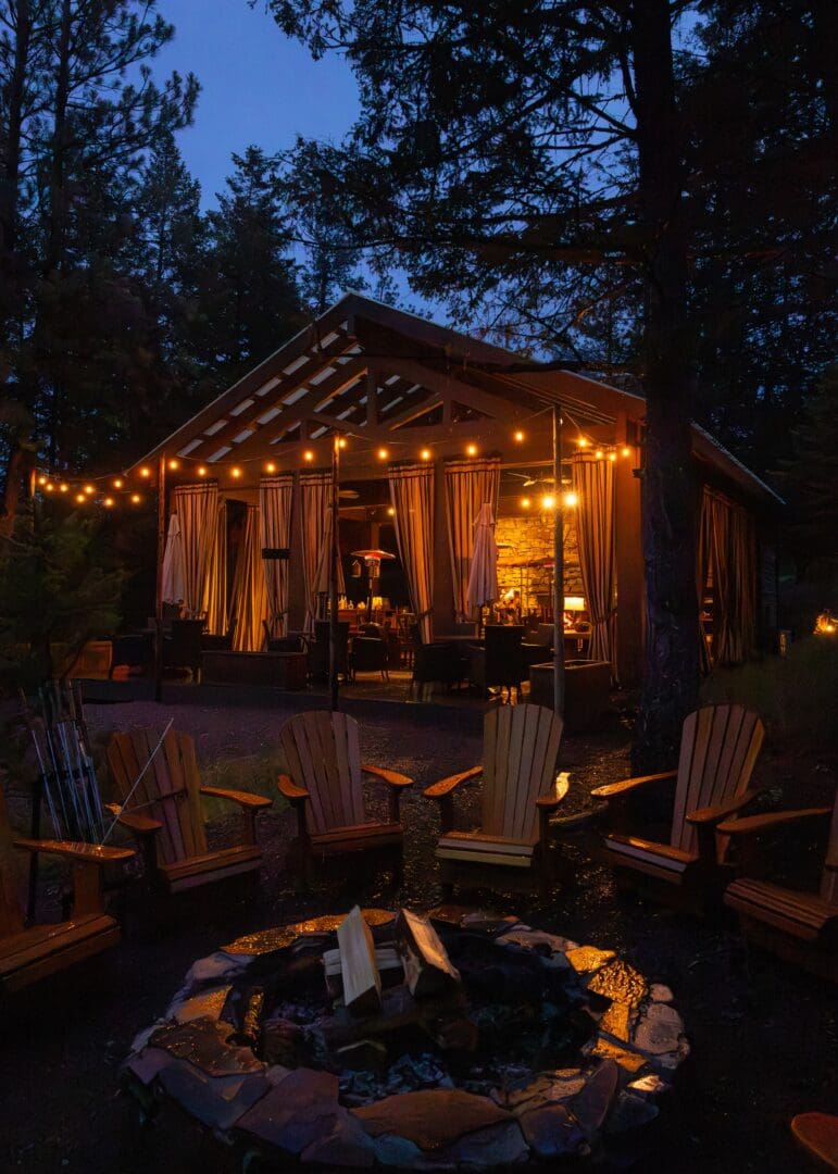 Lit up pavilion with chairs surrounding an outdoor fireplace.