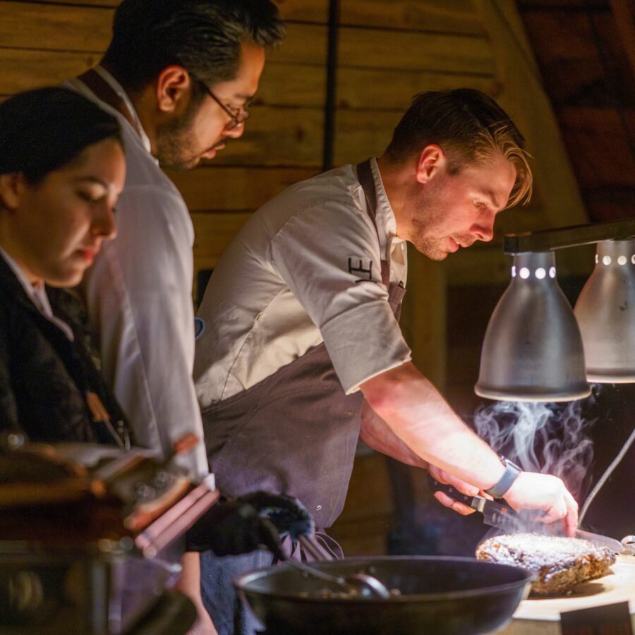 Three chefs setting up food under heat lamps.