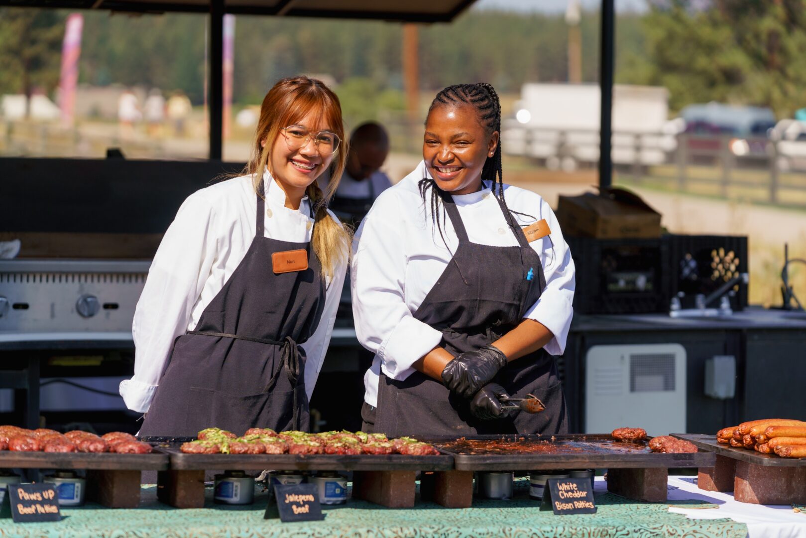 Two staff members serving food outside with black aprons and white shirts.