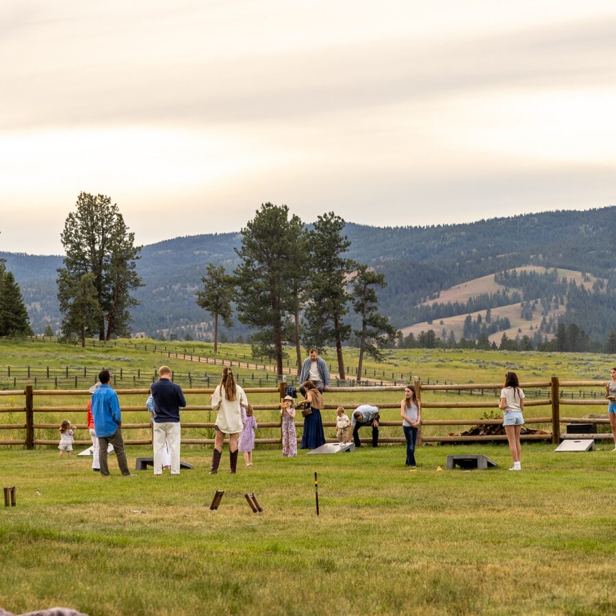 Family playing games on a green lawn with a wooden fence and field behind them.