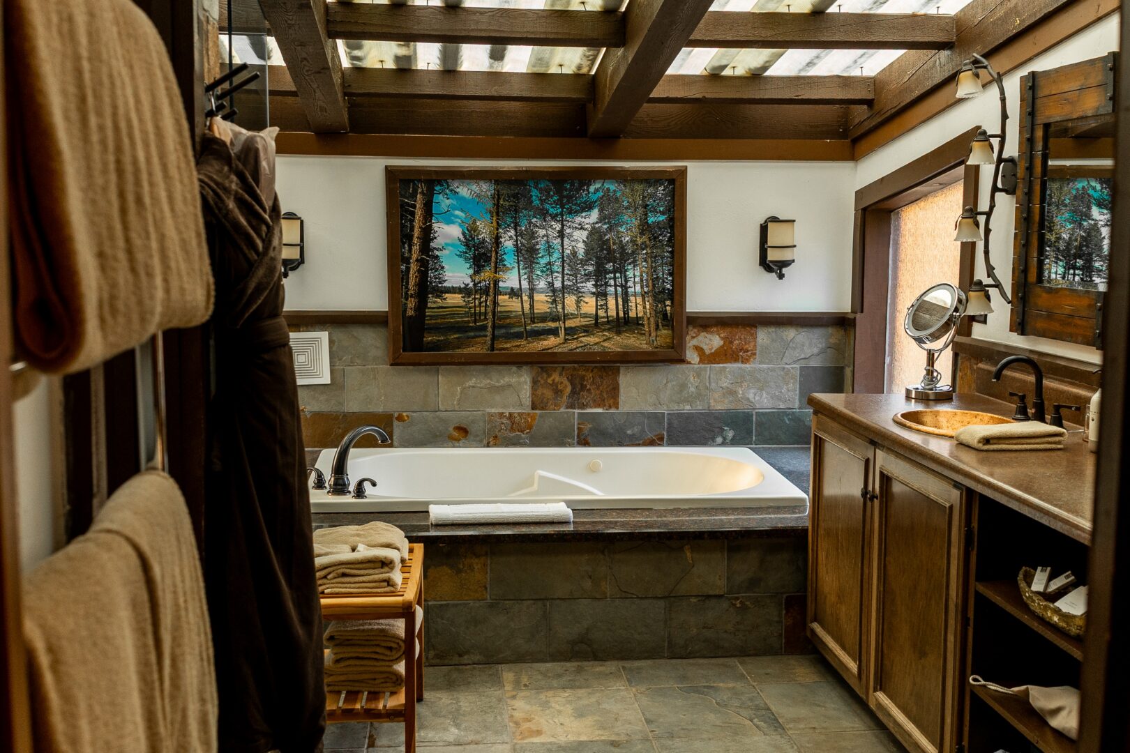 A well-appointed bathroom with a large, rectangular bathtub positioned centrally. Above the tub, there is a framed painting depicting a serene forest scene.